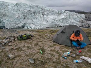 ACT_D1-2 Man camping in his tent on the ground infront of the Greenland ice-cap edge.