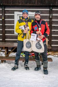 Two guys with gold medal from the dogsledrace infront of the wooden house