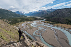 El Chalten circuit (3 of 14) meandering river in the wide valley with snowy peaks in the background. A guy standing on the edge of the cliff falling into the river