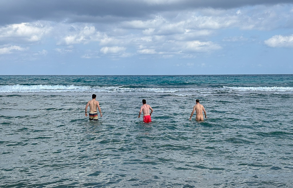 Tři muži, kteří se koupají v moři nazí
