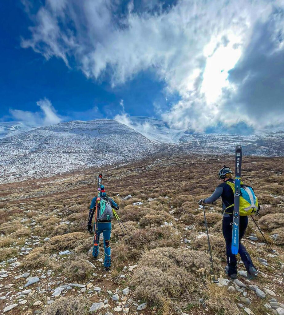 Lyžaři s lyžemi na batohu kráčející k hranici sněhu