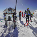 A skimo racer next to the bell on top of the mountain Ida