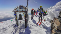 A skimo racer next to the bell on top of the mountain Ida