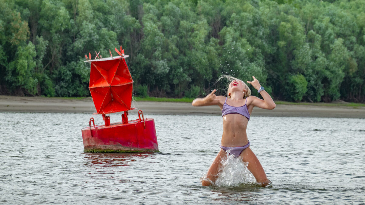 Girl jumping on the beach near navigation buoy on the Donau River